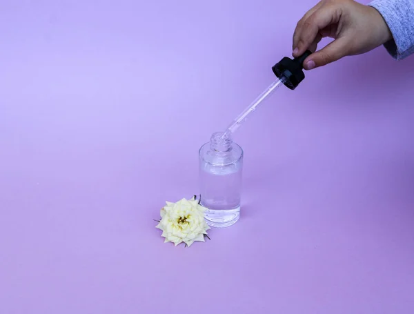 Скляна пляшка з піпеткою з олією або сироваткою, з квіткою білої троянди на тонкому фоні. Концепція: органічна біокосметика, рослинні олії, сироватковий колаген, догляд за шкірою — стокове фото