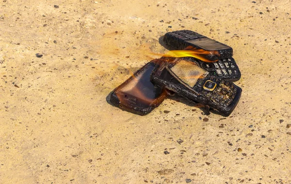 Dokusal beton arka plan üzerinde yanmış cep telefonları. Konsept: Düşük kaliteli cep telefonları kullanma tehlikesi. — Stok fotoğraf