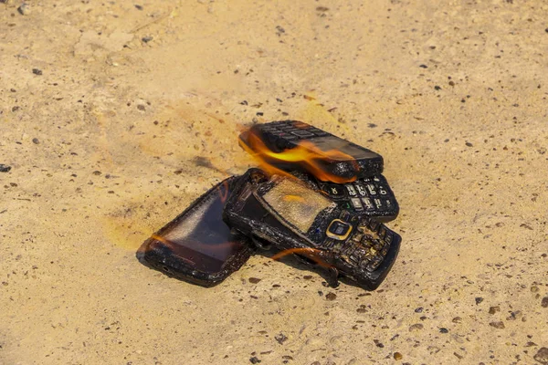 Teléfonos móviles quemados sobre fondo de hormigón texturizado. Concepto: Peligro de usar teléfonos celulares de baja calidad . — Foto de Stock