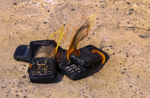 burnt mobile phones on textural concrete background. Concept: Danger of using low-quality cell phones.