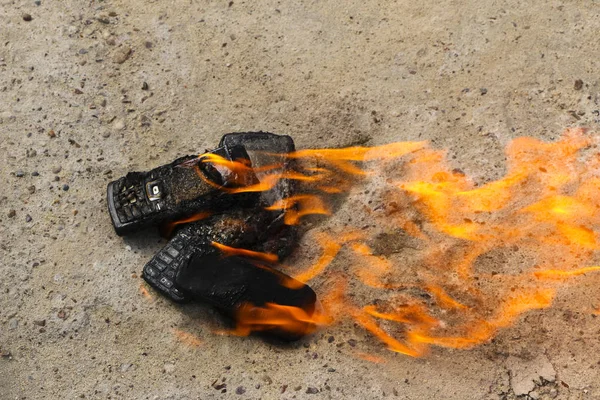 Burnt mobile phones on textural concrete background. Concept: Danger of using low-quality cell phones. — Stock Photo, Image