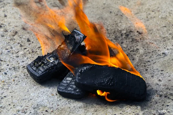 Teléfonos móviles quemados sobre fondo de hormigón texturizado. Concepto: Peligro de usar teléfonos celulares de baja calidad . — Foto de Stock