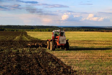 Traktör güneşli bir bahar gününde geniş bir tarlada tarlayı sürüp saklar. Toprağı ekin ekmeye hazırlamak, toprağı bir traktörle sürmek bir disk sabanı ile..