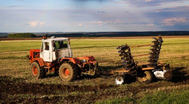 the tractor plows and harrows the land in a large field on a sunny spring day. preparing the soil for planting crops, plowing the soil with a tractor with a disk plow. clipart