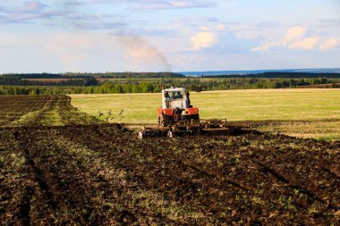 Traktör güneşli bir bahar gününde geniş bir tarlada tarlayı sürüp saklar. Toprağı ekin ekmeye hazırlamak, toprağı bir traktörle sürmek bir disk sabanı ile..