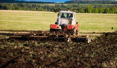 the tractor plows and harrows the land in a large field on a sunny spring day. preparing the soil for planting crops, plowing the soil with a tractor with a disk plow. clipart