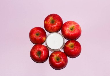 Kırmızı sulu elmalarla kozmetik kompozisyonu ve pembe arka planda beyaz yumuşak nemlendirici krem ile açık bir kavanoz..
