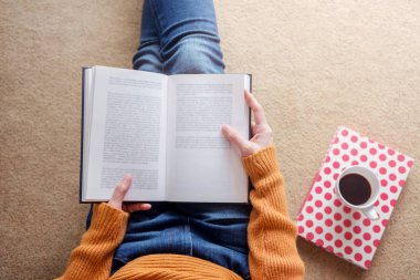 Okuma kavramı. Genç kadının rahatlatıcı kitap ve rahat evde kahve yumuşak odak ana sayfa görünümü