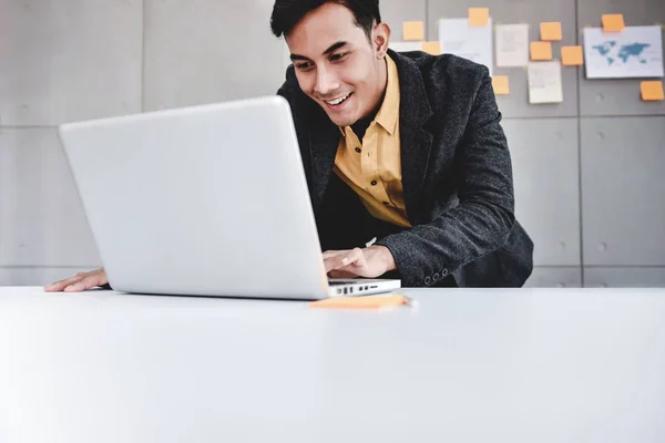 Χαρούμενος νεαρός Ασίας επιχειρηματίας που εργάζεται στον υπολογιστή φορητό υπολογιστή στο δημο — Φωτογραφία Αρχείου