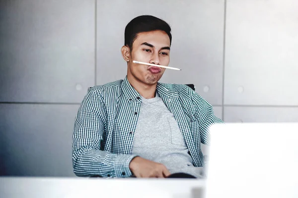 Figlarny Młody Biznesmen Trzymanie Pióra Między Nos Usta Praca Komputerze — Zdjęcie stockowe