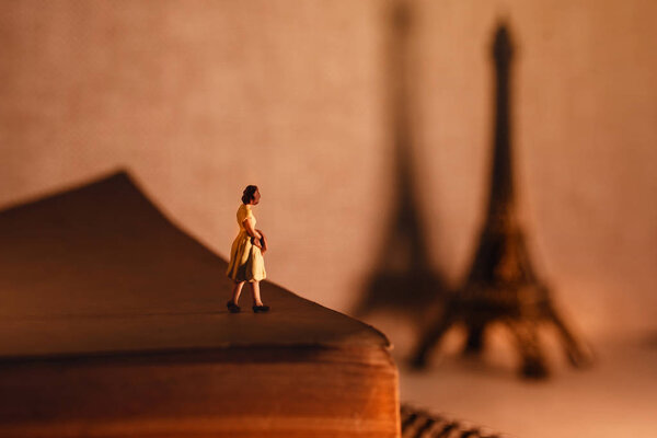 Dream Destination for Vacation. Travel in Paris, France. Figurine of Tourist Woman Standing on Aged Book and Looking at Eiffel Tower. Vintage Style