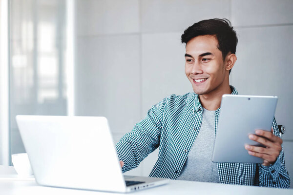 Happy Young Businessman Working on Computer Laptop and Digital Tablet in Office