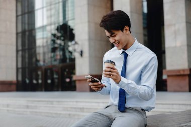 Gülümseyen Genç Asain İş Adamı Şehirde Cep Telefonu Kullanıyor