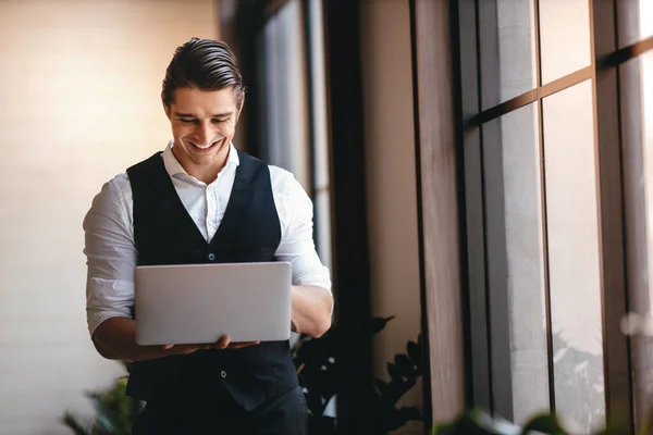 一位年轻的白种人商人在现代工作场所的电脑笔记本电脑上工作 微笑的商人站在窗边 — 图库照片