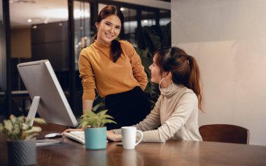 Takım çalışması, birlikte çalışmak. Modern Ofiste Bilgisayarda İki İş Kadını Gülümsüyor. Ana model kameraya bakıyor.