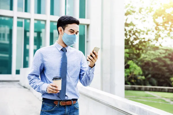 在城市里 年轻的亚洲商人戴着外科面具 使用智能手机 新的正常生活方式概念中的医疗保健 — 图库照片