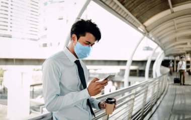 Genç Asyalı İş Adamı Cerrahi Maske Takıyor ve Şehirde Akıllı Telefon Kullanıyor. Yeni Normal Yaşam Tarzı Konseptinde Sağlık Hizmetleri