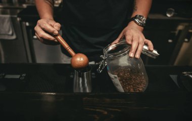 Kafede kahve yapan bir barista. Kahve çekirdeklerini ölçmek için tahta kaşık kullanıyor.