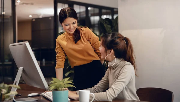 Teamwork, Working Together. Smiling Two Business Woman Workigng on Computer in Modern Office. Looking each other. Happy Relationship between Boss and Employee
