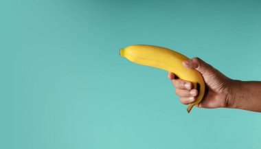 Muz kavramı görüntüsü. Mavi arka planda muz tutarken silah gibi görünürdü. Metafor Fotoğrafı. Temiz ve Asgari