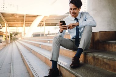 Şehirde cep telefonu kullanan gülümseyen Asyalı genç iş adamı. Merdiven 'de oturuyor.