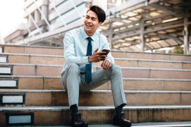 Şehirde cep telefonu kullanan gülümseyen Asyalı genç iş adamı. Merdiven 'de oturuyor.