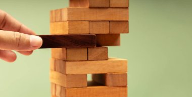 hand pulls a block from stack of Jenga tower. Emergency funds and money, business risk management