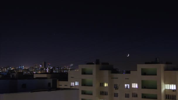 A cronologia da cidade noturna. Estrelas e lua nova se movem no céu.As janelas dos apartamentos residenciais acendem e se desligam. skyline cidade com edifícios altos — Vídeo de Stock