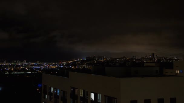 夜城天际线延时。从塔屋顶欣赏现代城市的顶级空中全景。路通。灯光在窗户中闪烁。浓密的云层在黑暗的天空中快速移动 — 图库视频影像
