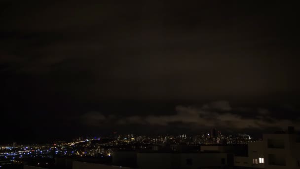 Ночная городская панорама. С крыши башни открывается панорамный вид на современный город. Дорожное движение. В окнах мерцают огни. Тяжелые облака быстро движутся в темном небе — стоковое видео