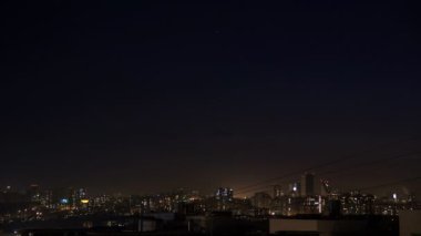 Gece şehir silueti timelapse. Kule çatıdan modern şehrin üst hava panoramik görünümü. Pencerelerde ışıklar titriyor. Yıldızlar karanlık gökyüzünde hareket
