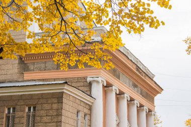 Sütunlu tiyatro binasının çatısı, altın yapraklı dal. Sonbahar arka planı