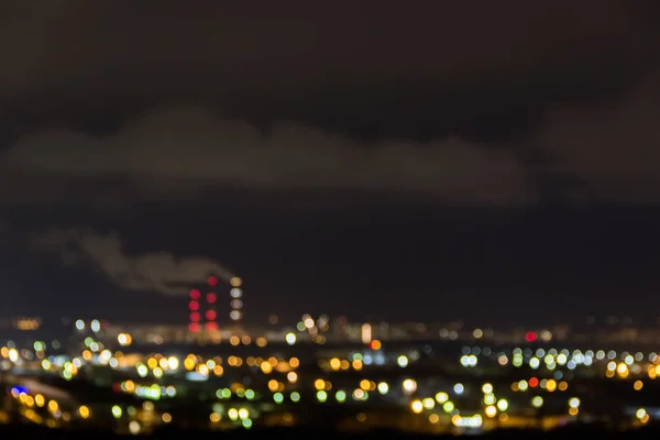 Skyline van de stad 's nachts. Nachtzicht van een buurt met laagbouw appartement blokkeert verlichte raam lampjes. Leidingen van rook van thermische energiecentrales. Wazig abstract beeld van industriële zone — Stockfoto