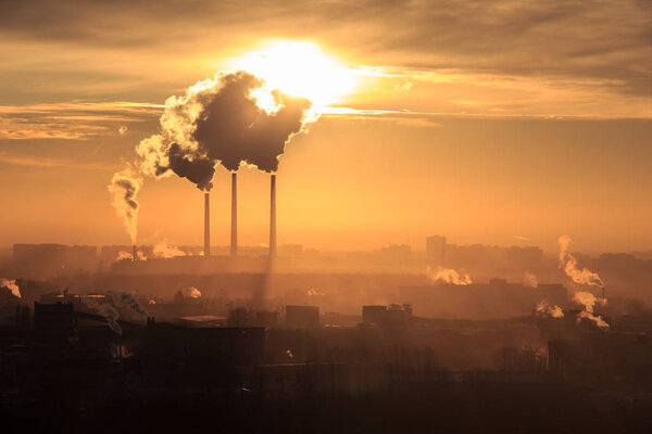 Roofs of city houses during sunrise.Dark smoke coming from the thermal power plant pipe. Factory smoke, polluting the atmosphere. Industrial zone in the city