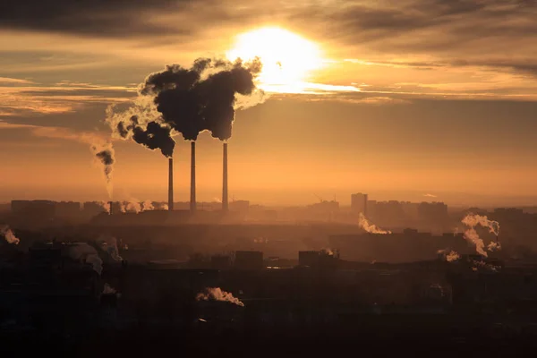 Dachy domów miejskich podczas wschodu słońca. Ciemny dym pochodzący z rury elektrowni cieplnej. Dym fabryczny, zanieczyszczający atmosferę. Strefa przemysłowa w mieście — Zdjęcie stockowe