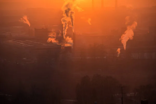Salida del sol sobre la fábrica en el área industrial. Los rayos de luz naranja vienen a través de la niebla matutina y humo de tuberías. Fabricación química industrial —  Fotos de Stock