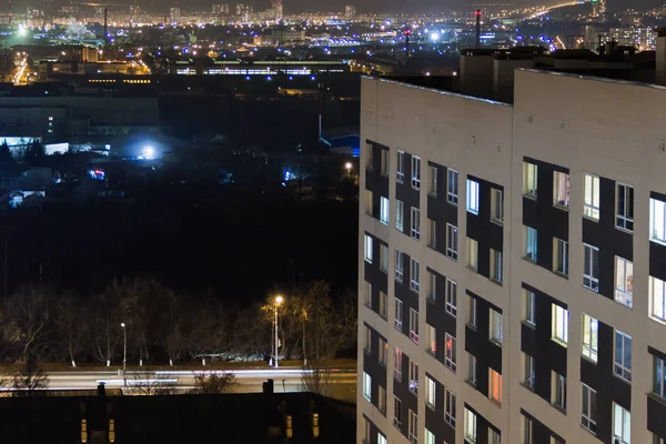 Hoogbouw modern gebouw in het avond raam lichten. Casual stedelijk stadsleven. Verkeer op de weg. — Stockfoto