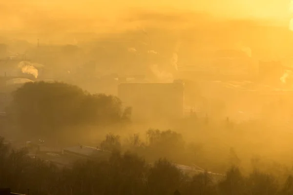 Nebliger Morgen in der Stadt. Sonnenaufgang über der nebligen Stadt. Nebelschwaden bedecken Gebäude, Fabrikrohre und Bäume — Stockfoto