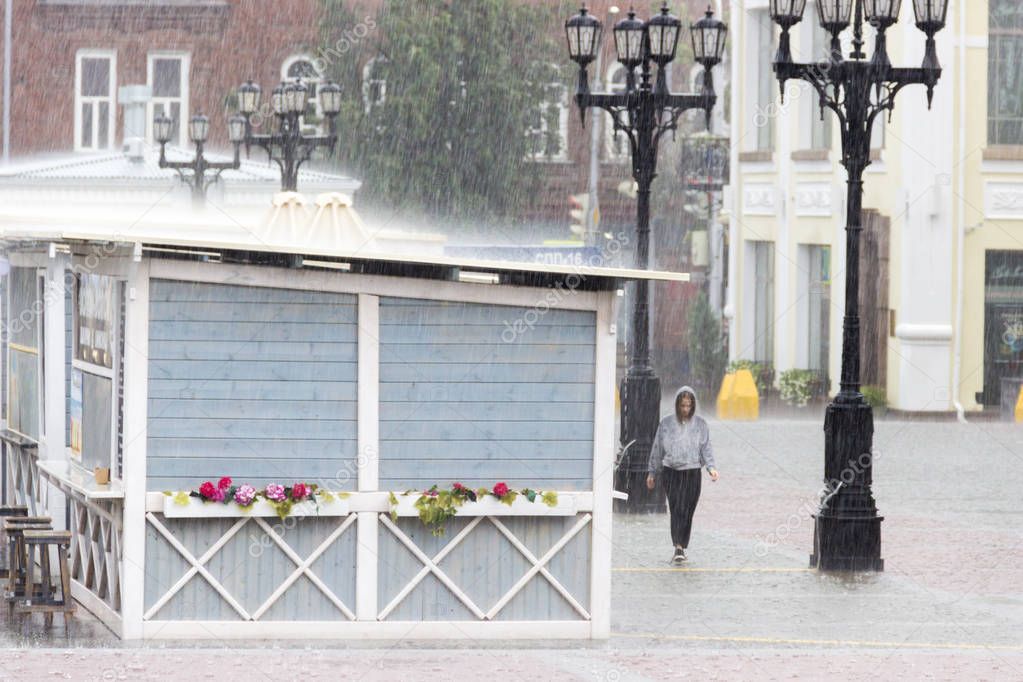 Rain in the city. Wooden summer cafe on city square with retro streetlights. Wet girl in hoodie under rain