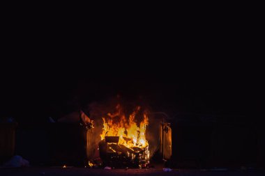 Yanan çöp konteyneri ve eski ahşap sandalye ile diğer çöp yakın. Plastik çöp tenekesi neredeyse erimiş