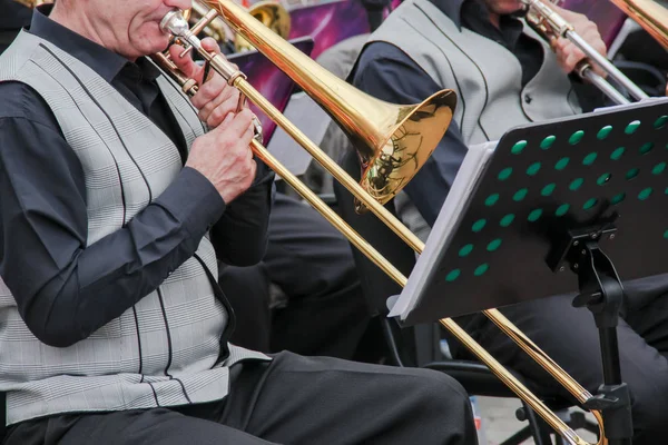 Viejo músico vestido con chaleco clásico de hombre tocando en un trombón en una orquesta, la música está detrás de él . — Foto de Stock