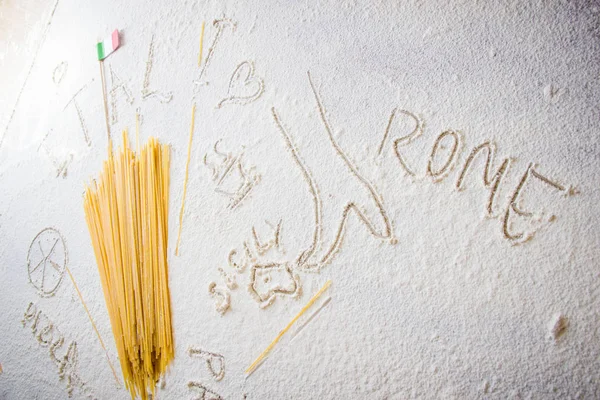 Uncooked pasta spaghetti macaroni and italian flag on floured white background. Words Italy, Rome, Sicily and Pasta