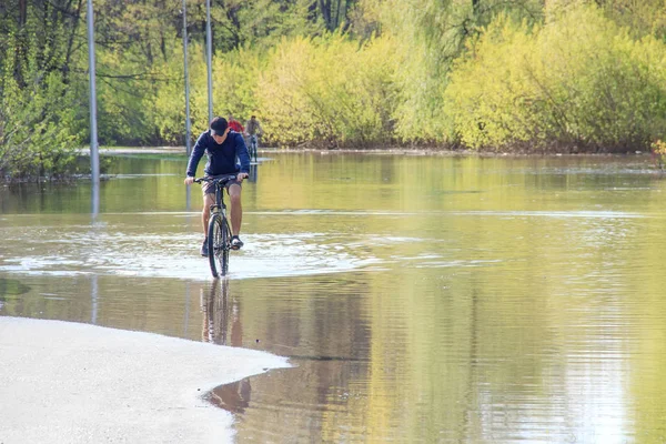 Велосипедист пытается ездить на велосипеде во время наводнения весной. асфальтовая дорога — стоковое фото