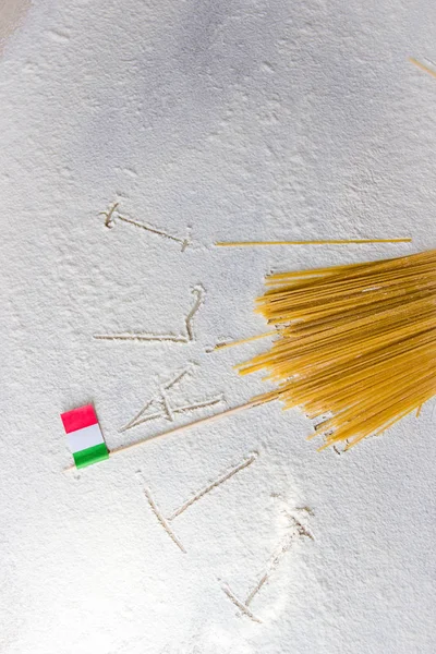 Italian food background, with raw spaghetti and italian flag. Itali sign written on flour from hand