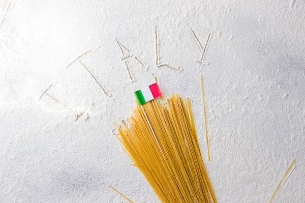 Italian food background, with raw spaghetti and italian flag. Italy sign written on flour from hand