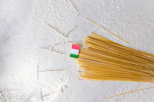 Italian food background, with raw spaghetti and italian flag. Italy sign written on flour from hand