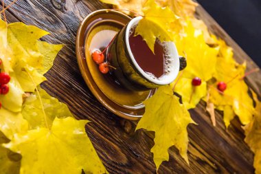 Tabakta koyu kahverengi bir fincan çay. Koyu kahverengi ahşap masa arka plan üzerinde sarı ve turuncu düşmüş akçaağaç yaprakları.