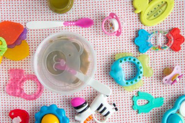 Masadaki pembe desenli bebek aksesuarları. Beslenmek için doğal sebze püresi ve gülümseyen ayı imajıyla kaşık ve bovling. Diş çıkaran oyuncaklar, kukla ve zebra çıngıraklı yılanı.