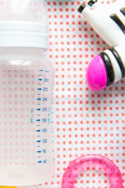 Masadaki pembe desenli bebek aksesuarları. Görüntüyü yakından beslemek için ölçeği olan boş bir şişe. Diş çıkartan oyuncaklar, çıngıraklı yılanlar.