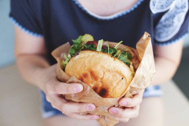 Kız büyük bir hamburger tutuyor. Yumuşak bulanık arkaplan. Yaşam tarzı